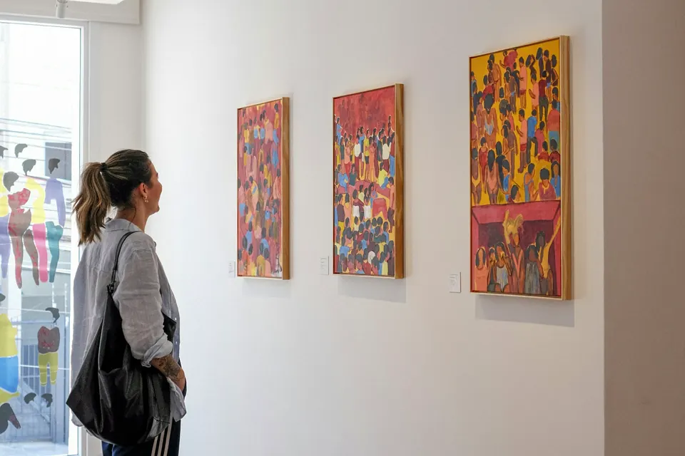 A visitor standing in a bright gallery, looking at a wall of colorful paintings
