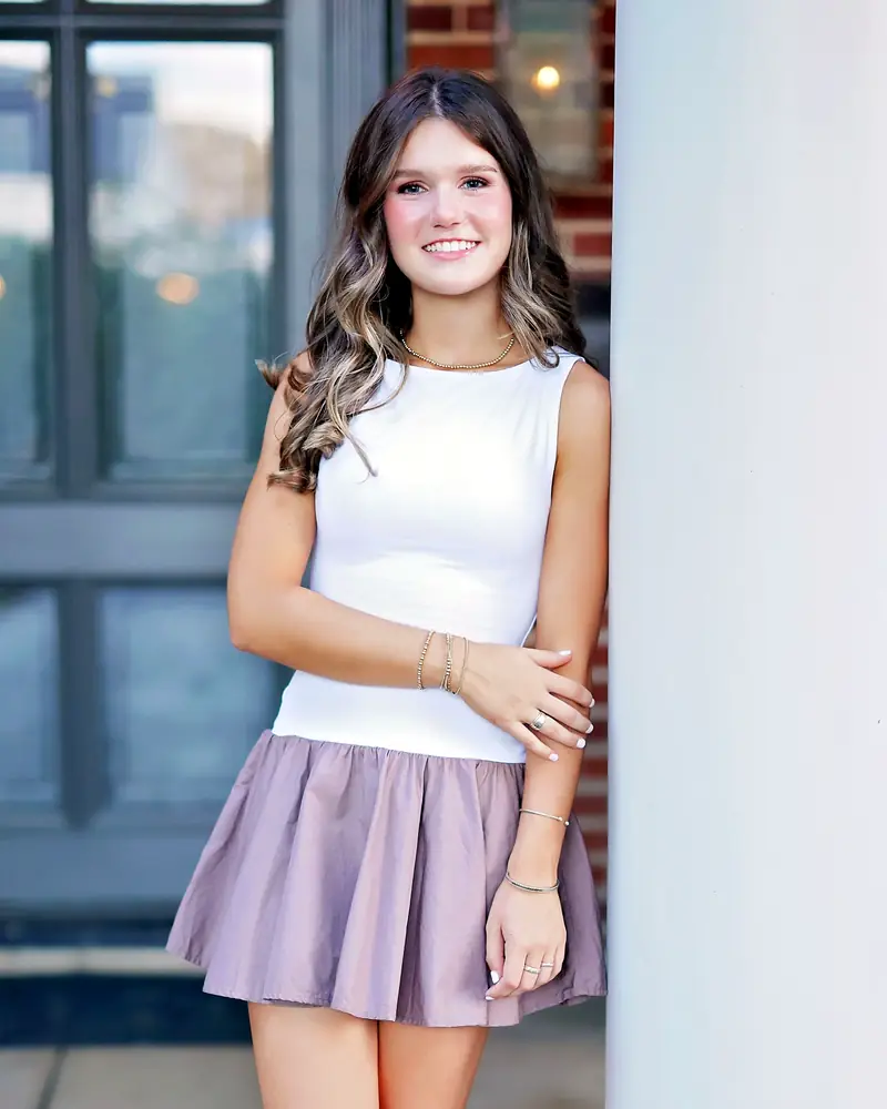 Lily Butler, the student artist behind Petri Palette, in a white top, leaning against a white column and smiling